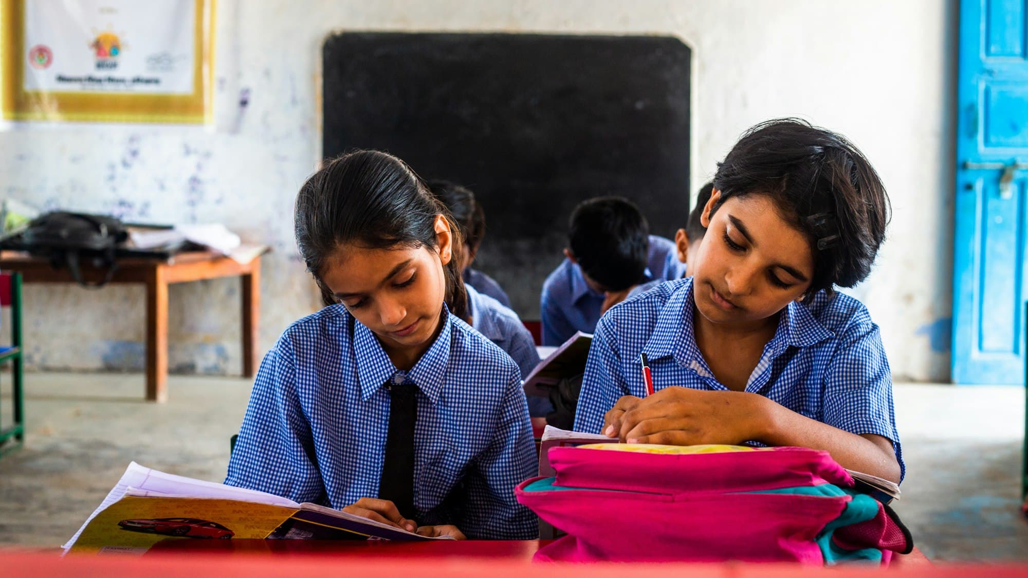 Two students in school uniform reading and writing at their classroom desk